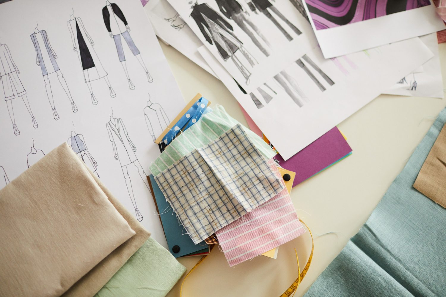 Close-up of samples of different fabric and sketches of new clothes collection on the table in workshop S